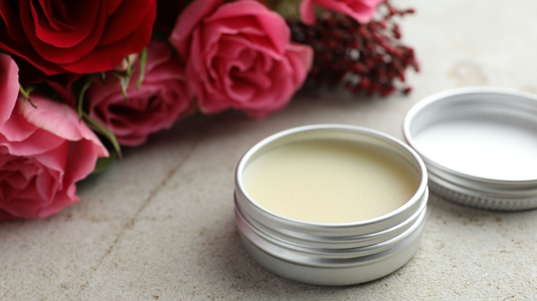 open cylinder container of solid perfume next to red roses